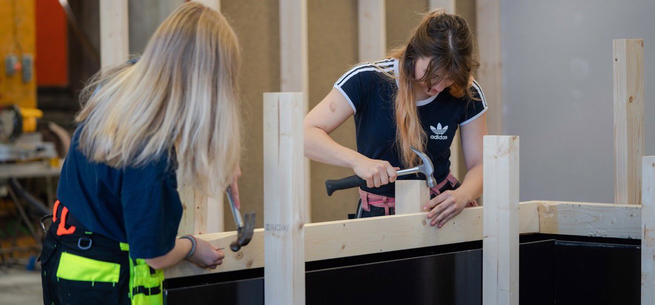  To jenter frå vg1 bygg- og anleggsteknikk byggjer ein trekonstruksjon med plankar, hammar og spikar.