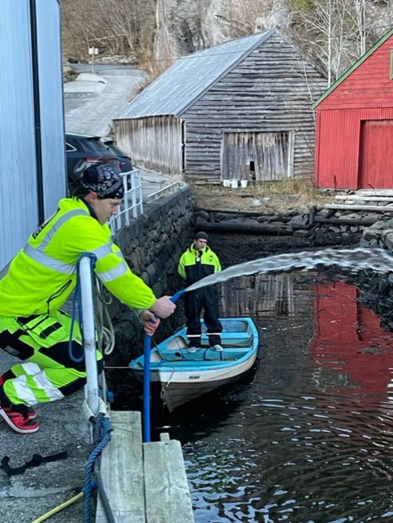 Skulebåten må vaskast, så ein elev spyler sida av båten med ein vannslange.