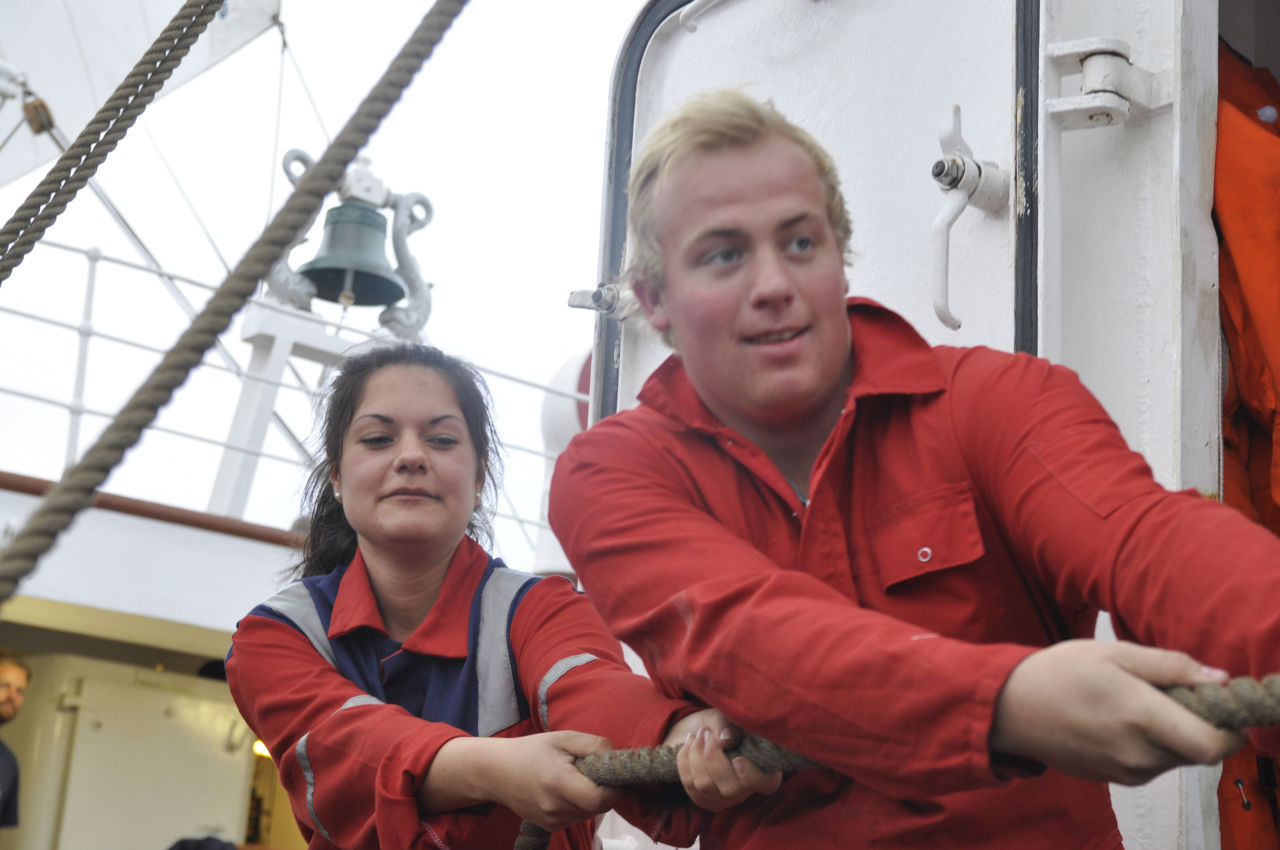 To elevar frå vg2 maritime fag er utplassert på seglskuta Statsråd Lemkul. Begge to dra i tauet(fallet) som heiser eit stort segl